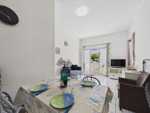 Ein Essbereich mit Tisch für zwei Personen, einer Couch, einem Fernseher und Blick ins Freie.