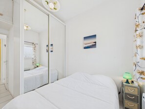 Een slaapkamer met een bed, een nachtkastje met een lamp, een spiegel en een aan de muur hangend schilderij.