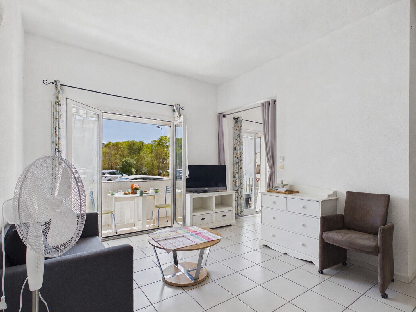 A room with a TV, a fan, a dining table, and a chair.