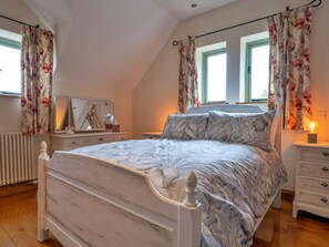 Ein Schlafzimmer mit Bett, Kommode, Spiegel und Vorhängen.