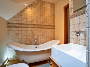 Ein Badezimmer mit freistehender Badewanne, einem separaten Waschbecken und einer gefliesten Wand.