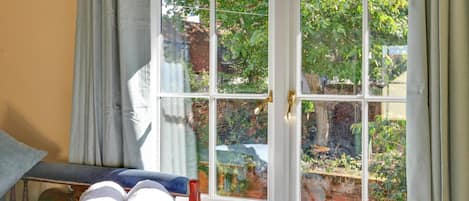 A room with a bed, a window with a view of greenery, and rolled towels on the bed.