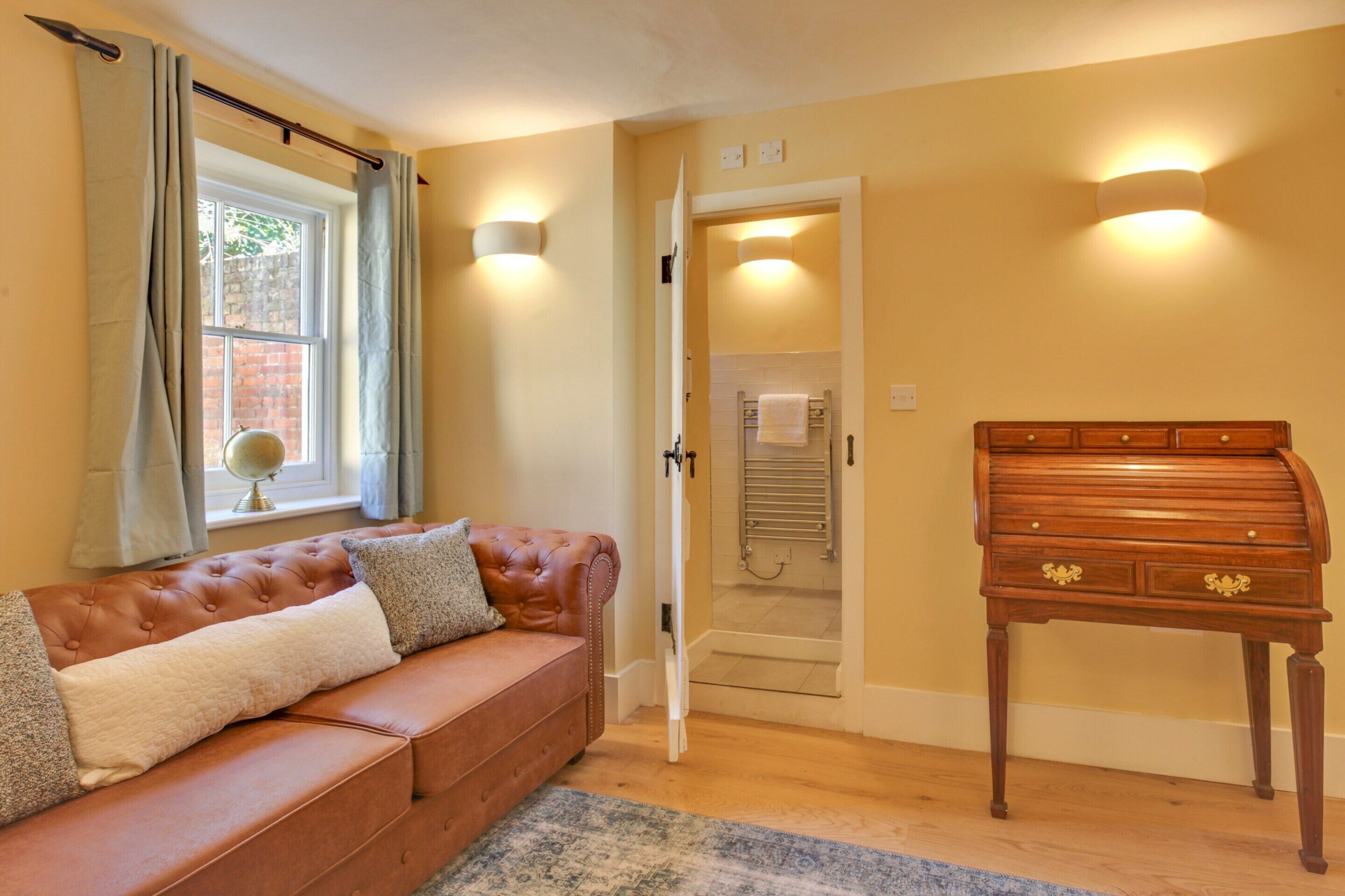 A room with a brown leather sofa, a wooden chest of drawers, and a window with curtains.