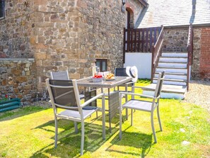 An outdoor patio with a stone wall, a wooden staircase, and a table with chairs. - Home Near Widemouth Bay (Bude)