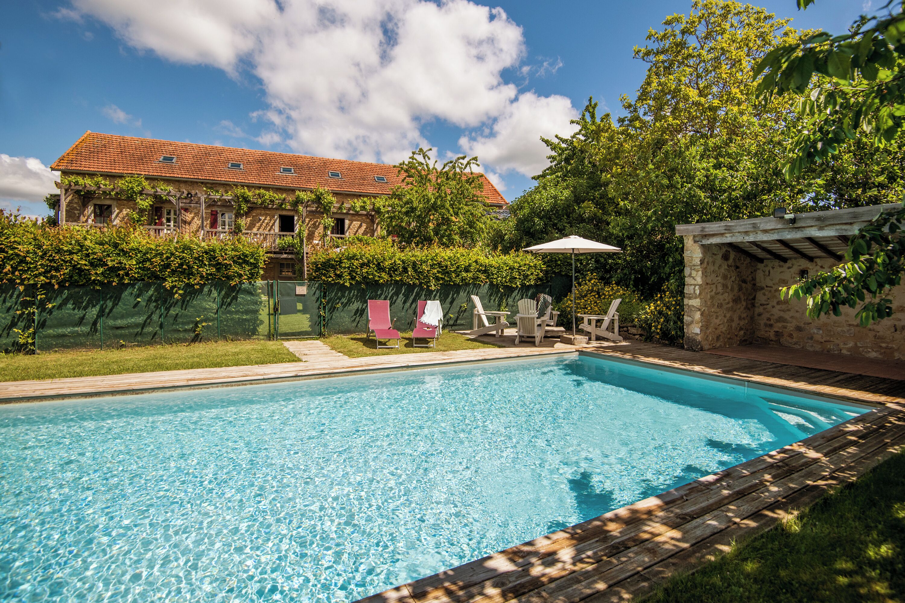 A swimming pool with lounge chairs, a pergola, and a stone wall.