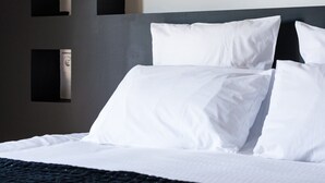 A neatly made bed with white linens in a modern hotel room.