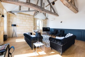 Ein geräumiges Wohnzimmer mit freiliegenden Holzbalken, einem großen Fenster und einem Fernseher.