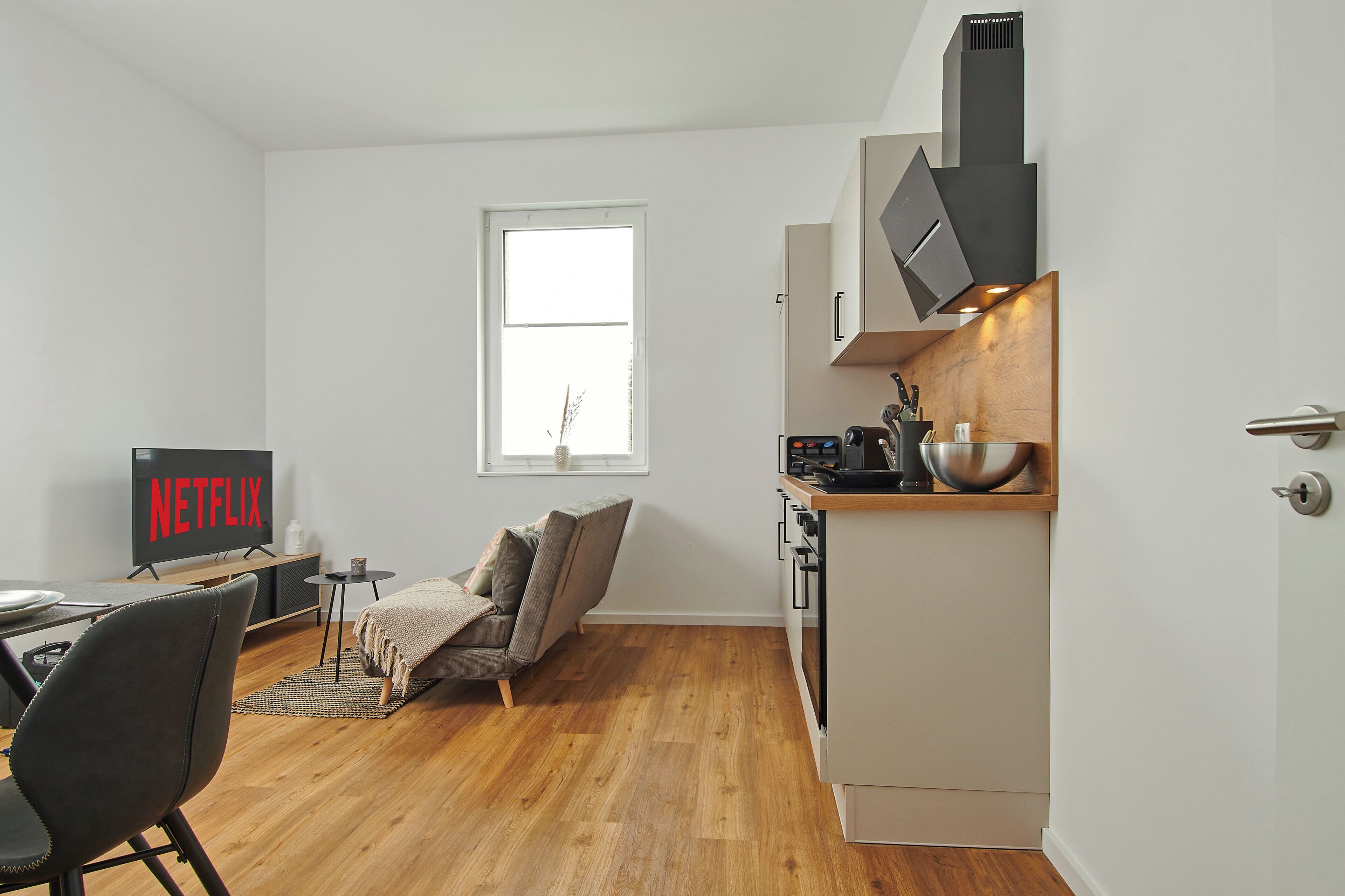 A compact living space with a kitchenette, a dining area, and a seating area with a television displaying 'NETFLIX'.