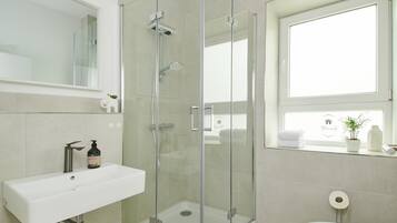 Et moderne badeværelse med en glasafskærmet brusekabine, en hvid vask og et toilet.