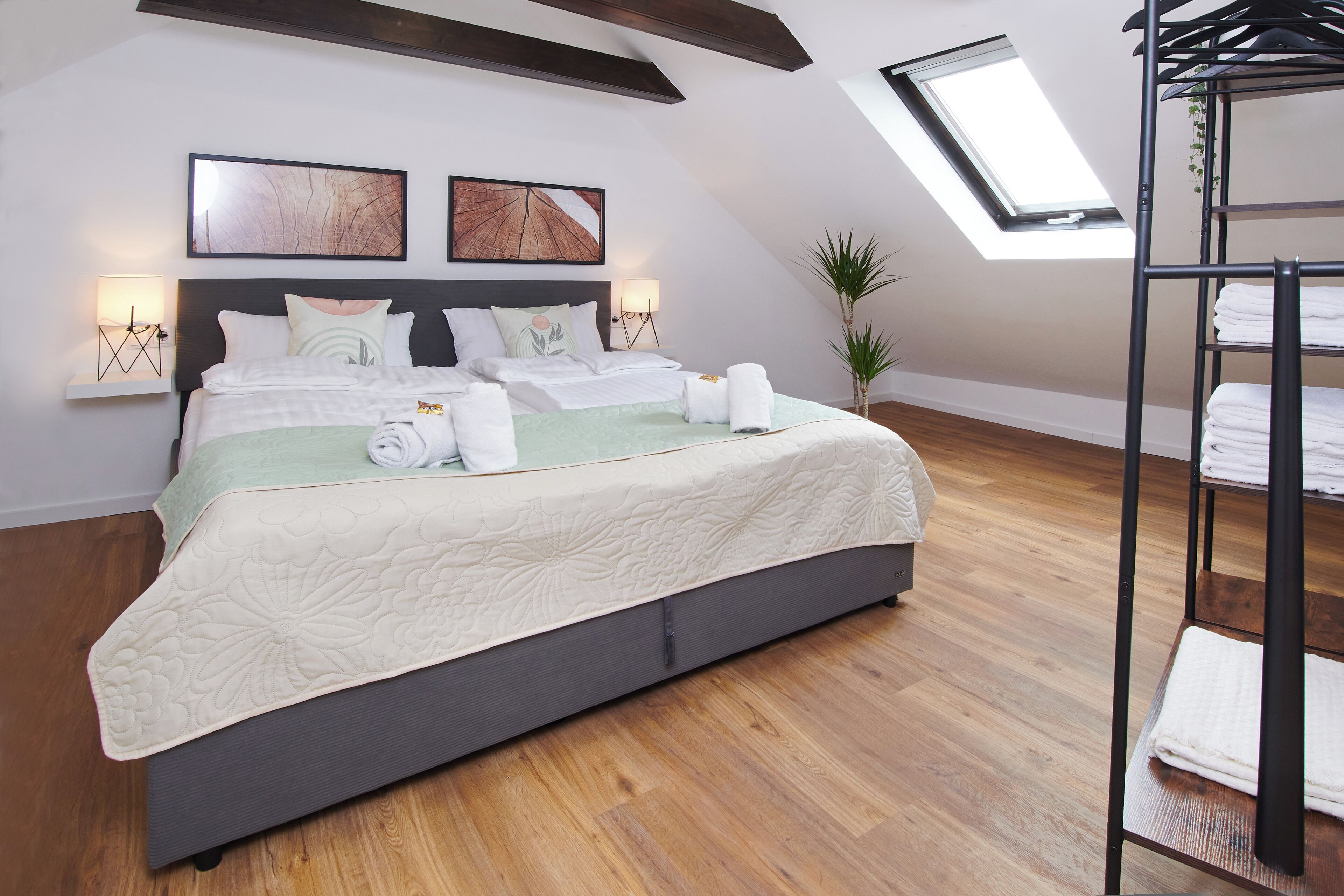 Une chambre moderne avec un grand lit, deux lampes fixées au mur, une lucarne et un plancher en bois.