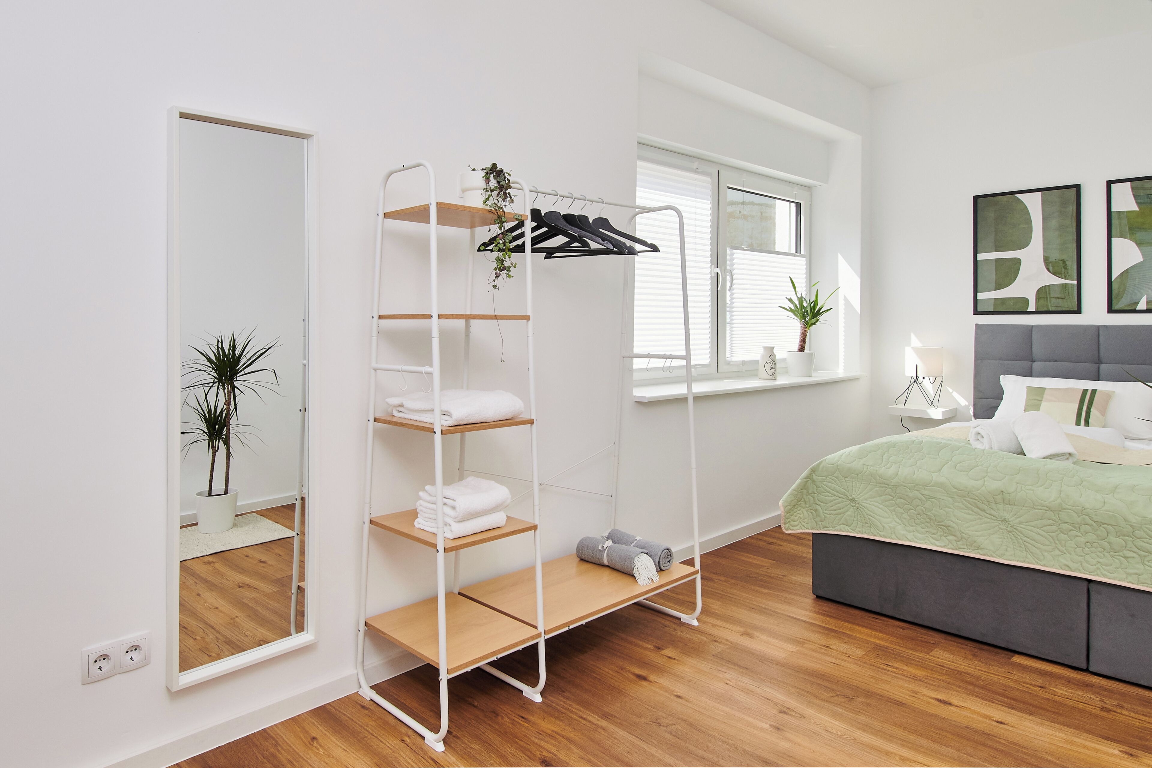 Ein modernes Schlafzimmer mit einem Bett, einem Schrank mit Regalen, einem Spiegel und einem Fenster mit Jalousien.