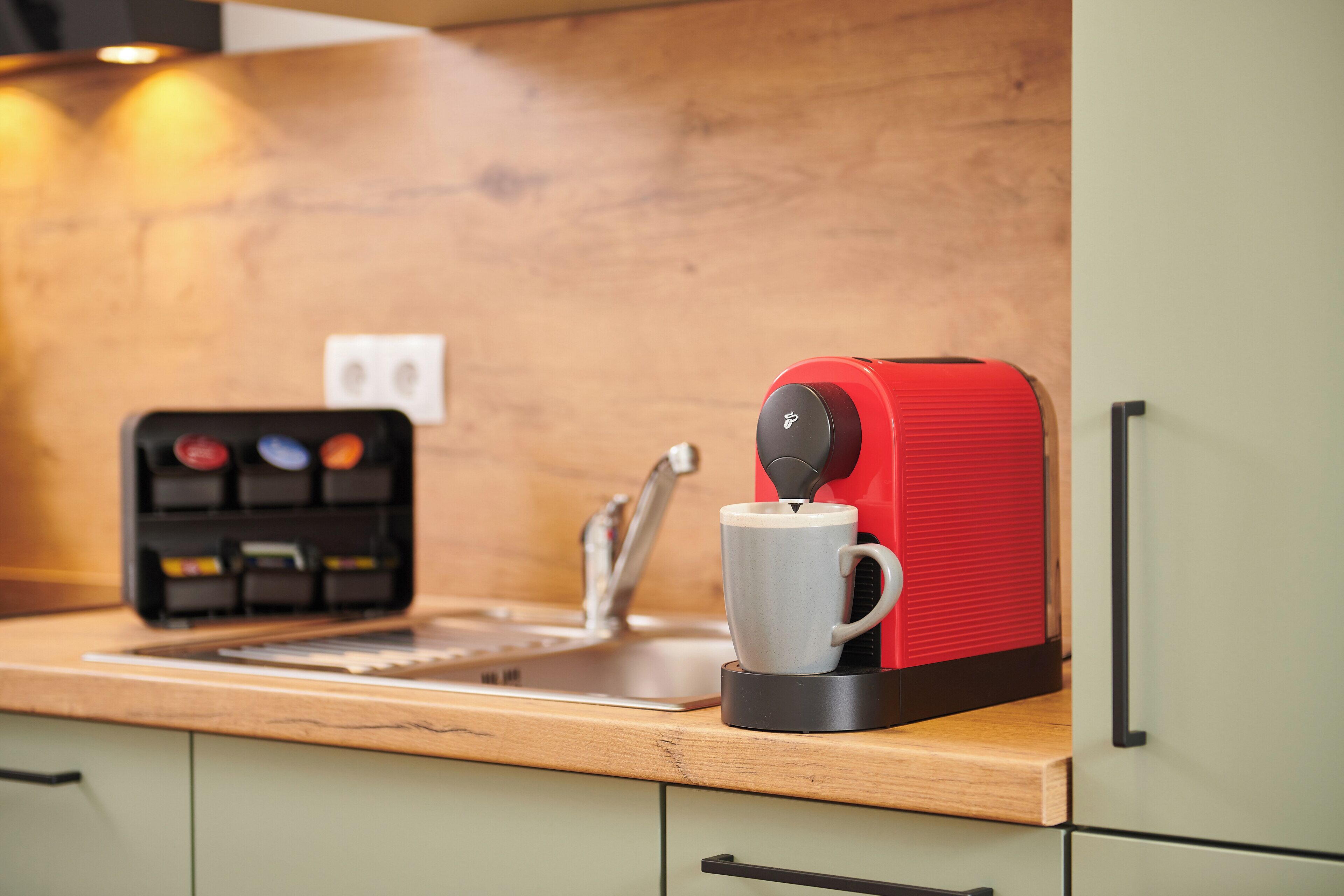 Une machine à café posée sur un comptoir en bois, avec une tasse et une cafetière.