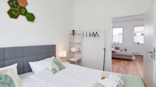 A hotel room with a bed, bedside tables, a wardrobe, and a view into the living area. - HomeME Bad Oeynhausen City (Bad Oeynhausen)