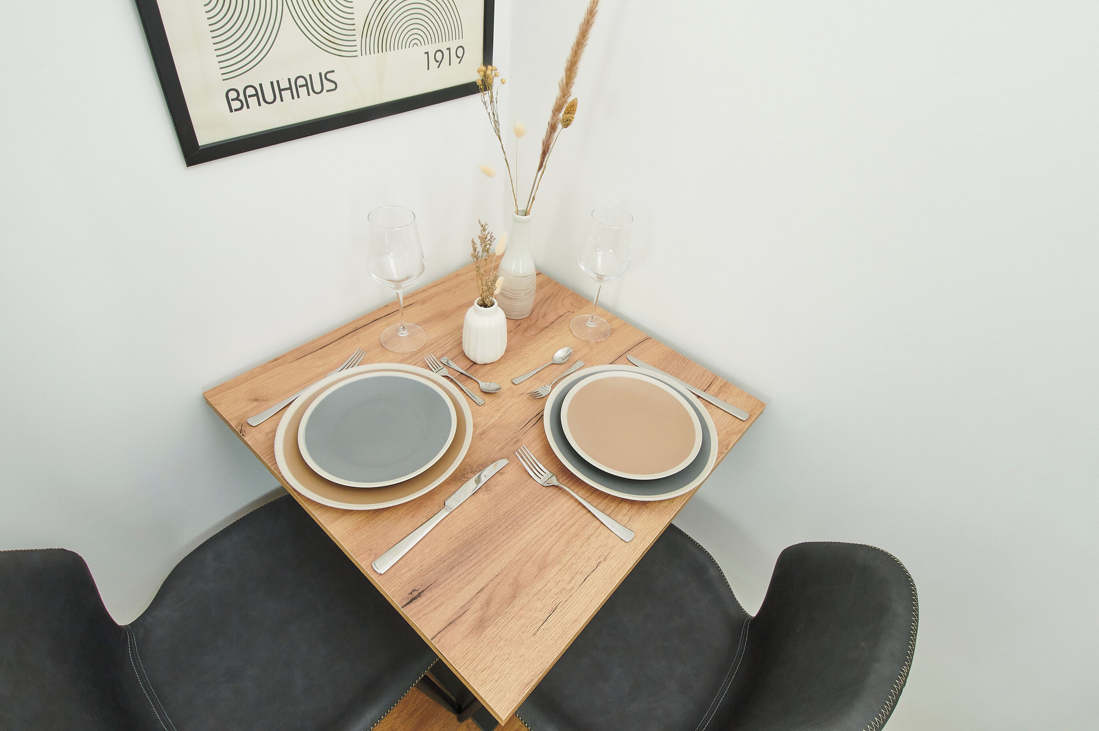 Une table à manger dressée avec des assiettes, des couverts et des verres, et un tableau encadré accroché au-dessus.