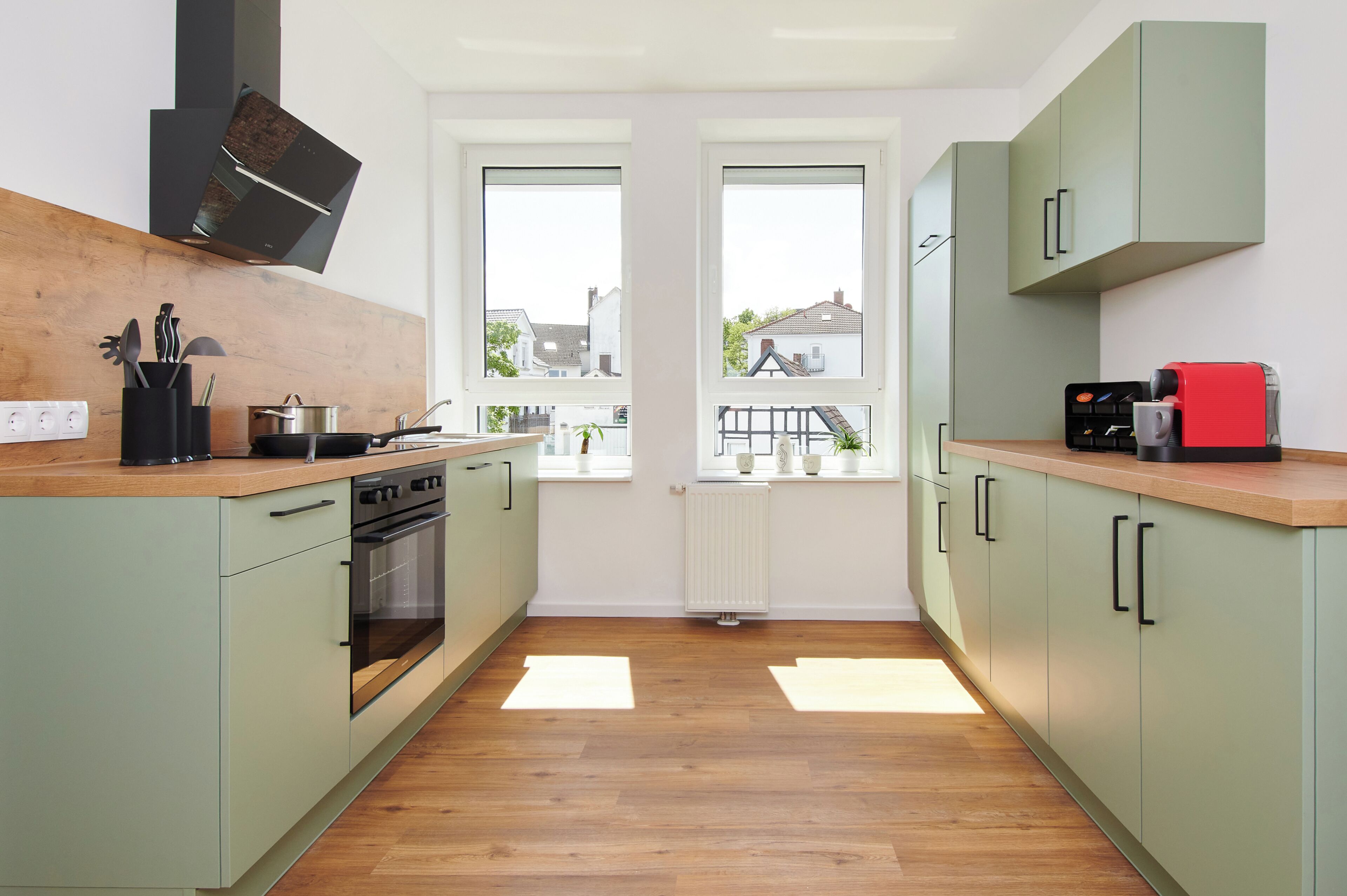 A modern kitchen with a built-in oven, a coffee machine, and a view of the outside through two windows.