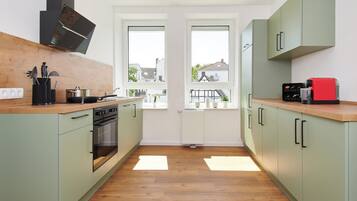 A modern kitchen with a built-in oven, a coffee machine, and a view of the outside through two windows.