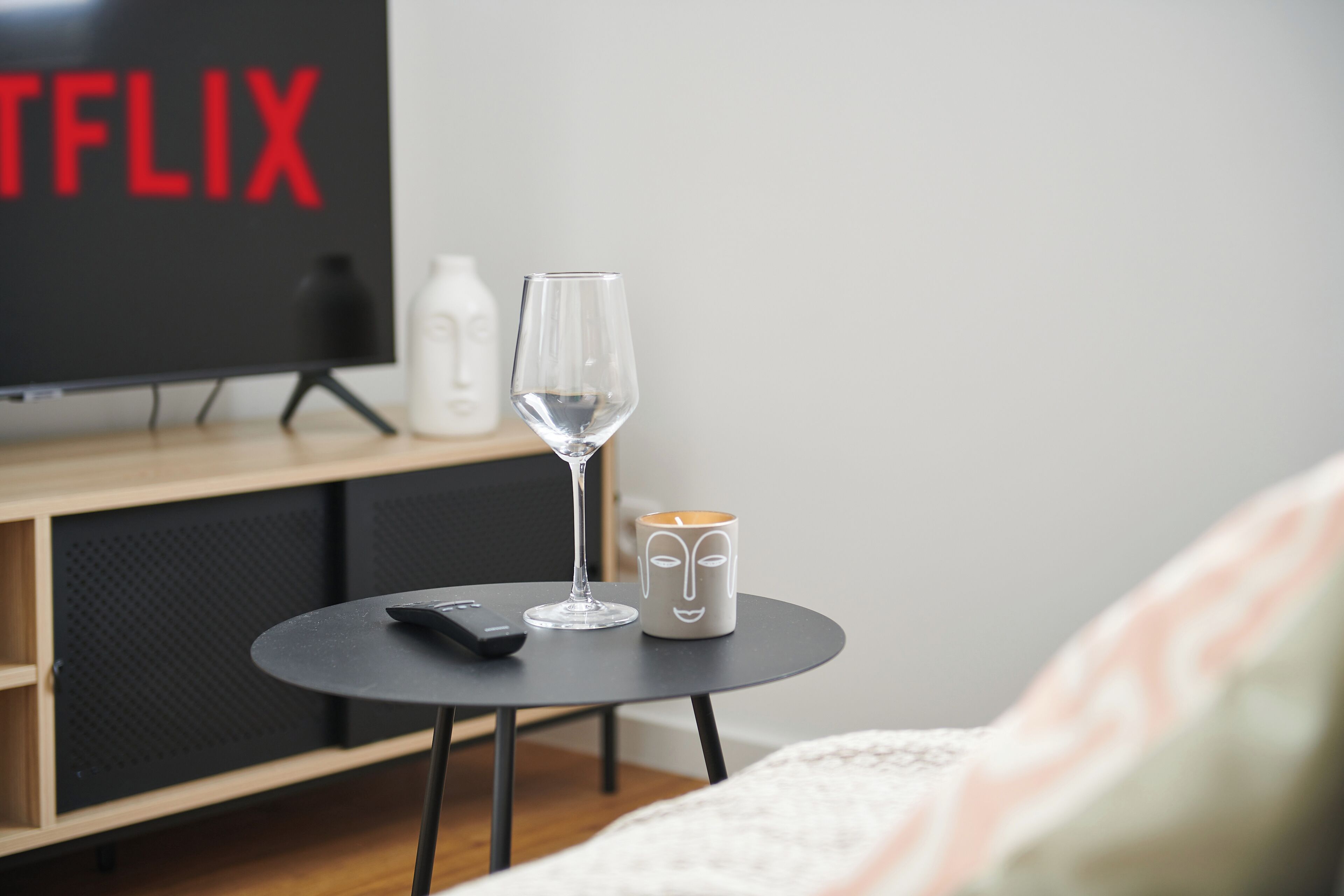 Habitación con un televisor mostrando el logo de Netflix, un vaso de agua, un control remoto y una taza con un diseño de rostro sobre una mesita.