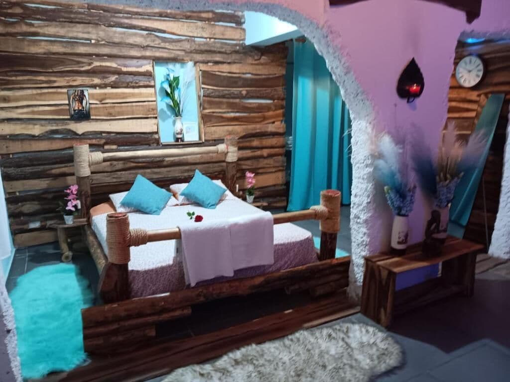 A rustic wooden room with a bed, a small table, and a wall clock.