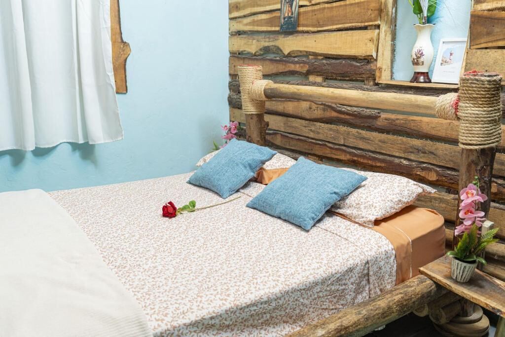 Een bed met een bloemenlaken, twee kussens, een rode roos en een houten hoofdbord.