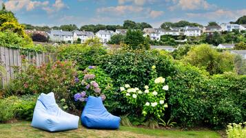 Un jardín con dos pufs azules, diversas plantas florecientes y una vista de casas al fondo.