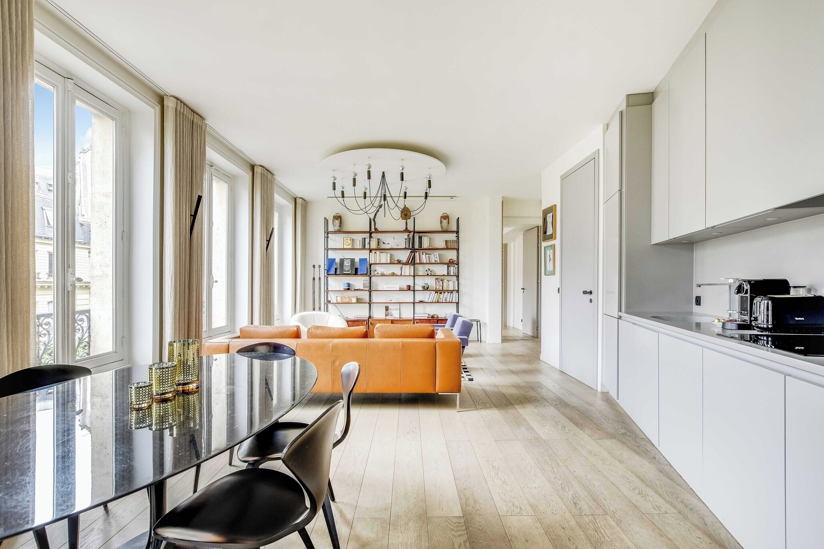 A modern kitchen with a dining area, a sofa, and a bookshelf.