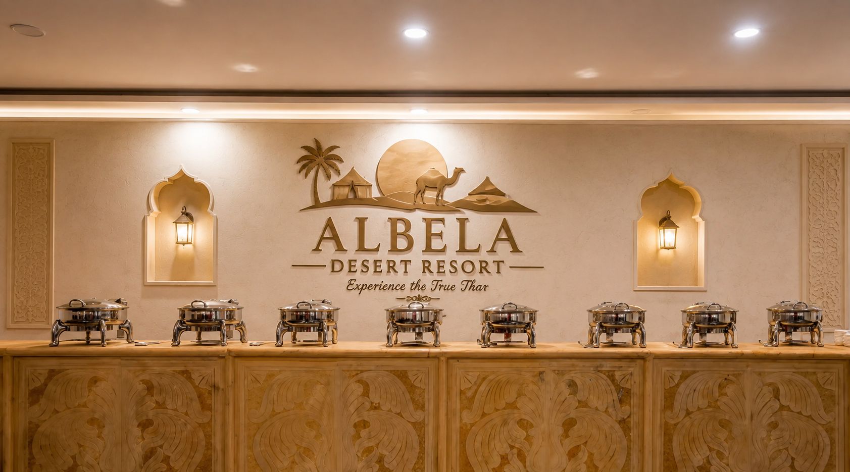 A reception area with a wall-mounted sign for Albela Desert Resort, featuring a desert scene and a camel. There are wall-mounted lights and a row of buffet service stations.