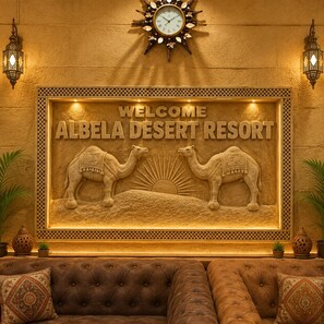 A wall with a welcome sign for Albelia Desert Resort, featuring two camels and a sun. - Albela Desert Resort  (Sam)