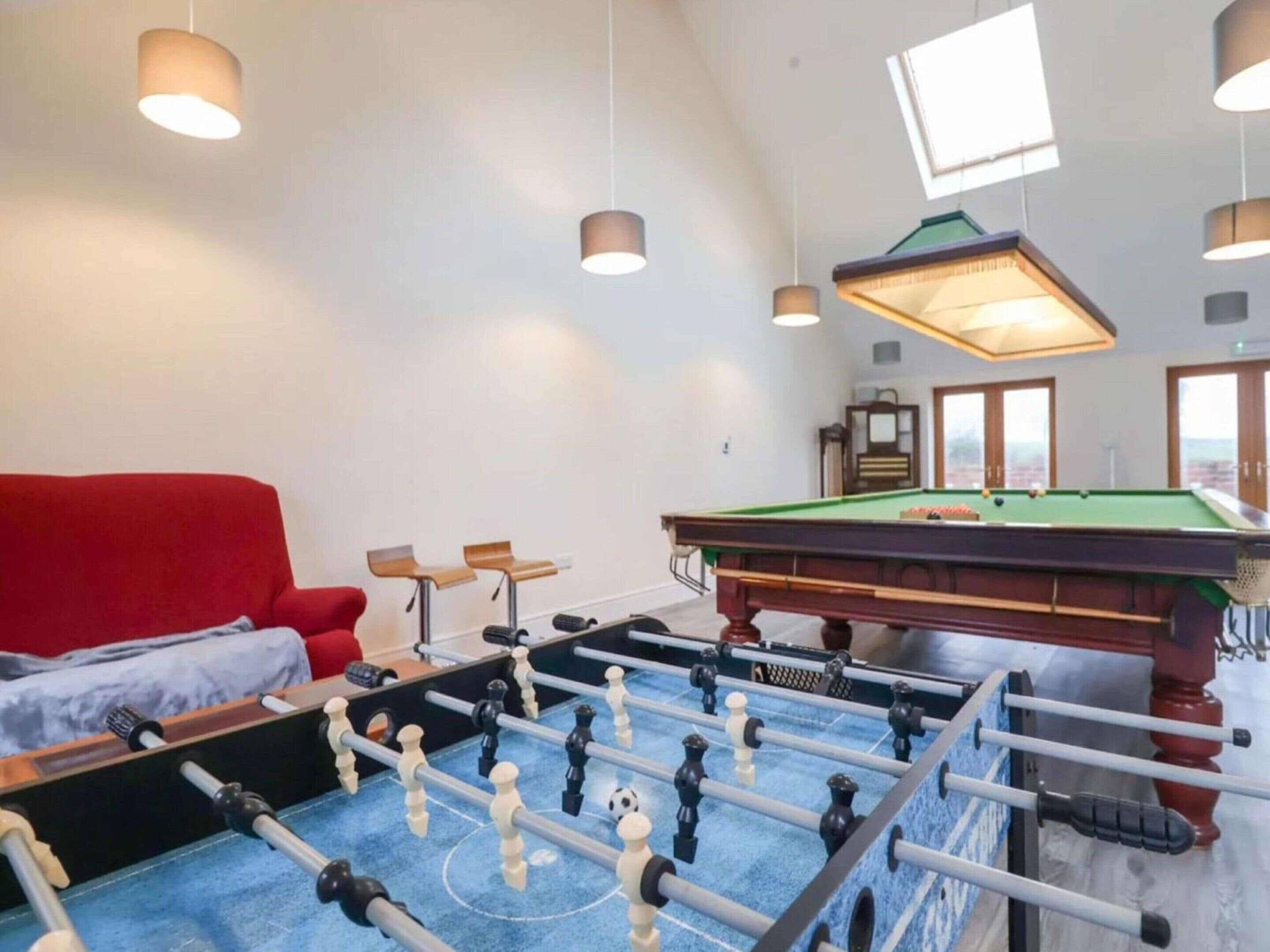 A room with a pool table, a red sofa, and a foosball table.