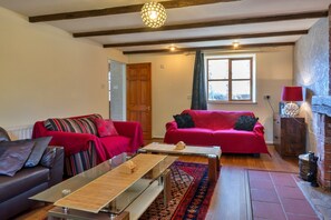 A living room with a red sofa, a brown sofa, a glass coffee table, a patterned rug, and a fireplace. - Spacious Devon Farmhouse (Exeter)