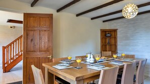 A dining area with a wooden table set for four, surrounded by chairs. A wooden cabinet with a teapot and cups is visible in the background. - Spacious Devon Farmhouse (Exeter)