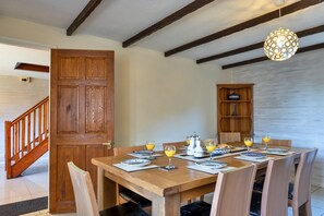 A dining area with a wooden table set for four, surrounded by chairs. A wooden cabinet with a teapot and cups is visible in the background. - Spacious Devon Farmhouse (Exeter)