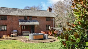 A brick house with a patio area, a hot tub, and a barbecue grill. - Spacious Devon Farmhouse (Exeter)