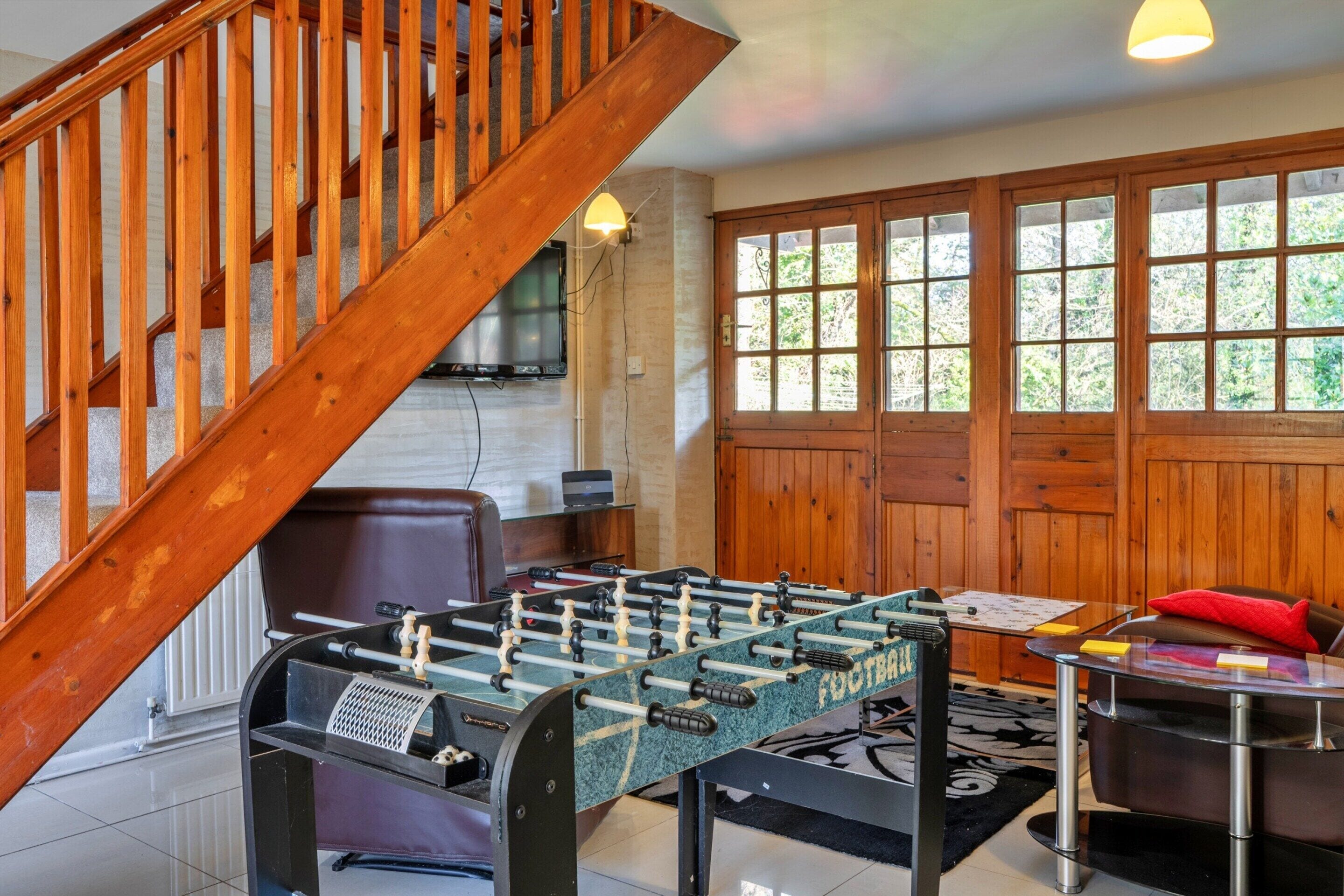 A room with a foosball table, a sofa, a coffee table, and a wooden staircase.