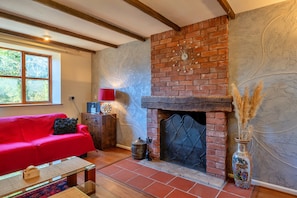 A room with a brick fireplace, a red sofa, a wooden coffee table, and a decorative vase. - Spacious Devon Farmhouse (Exeter)