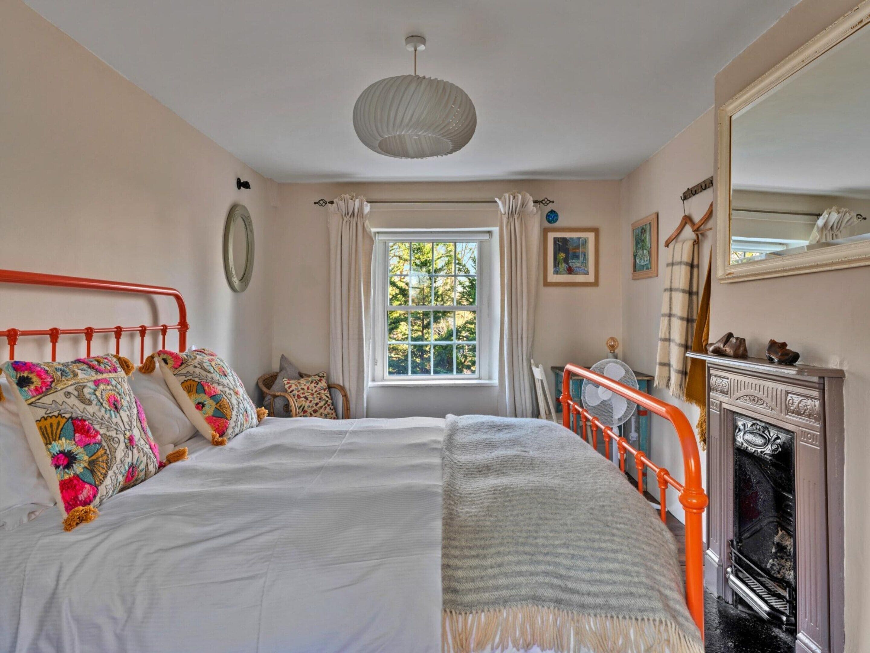 A bedroom with a bed, a window, a fireplace, and a mirror.