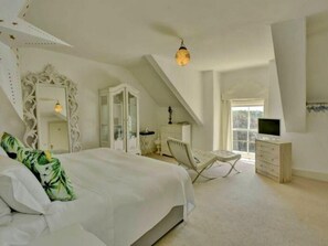 Ein Schlafzimmer mit einem großen Bett, einem Schminktisch, einem Sessel, einem Fernseher und einem Fenster.