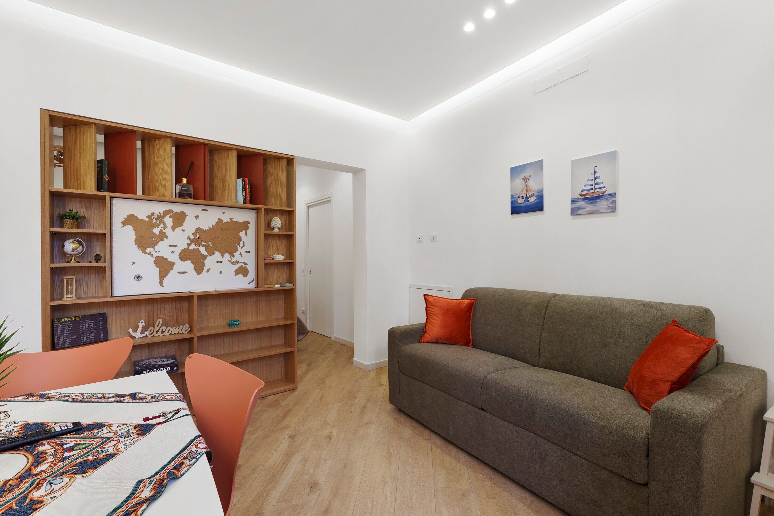 A living room with a grey sofa, orange pillows, a wooden bookshelf, and a world map on the wall.