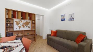 A living room with a grey sofa, orange pillows, a wooden bookshelf, and a world map on the wall.
