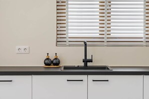 A kitchen with a black faucet, white cabinets, and a window with blinds. - Brisazou - Appartment 2 with 2 bedrooms (Willemstad)