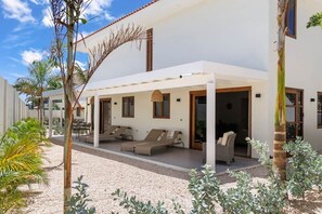 A covered outdoor seating area with lounge chairs and a table, surrounded by a gravel path and greenery. - Brisazou - Appartment 2 with 2 bedrooms (Willemstad)