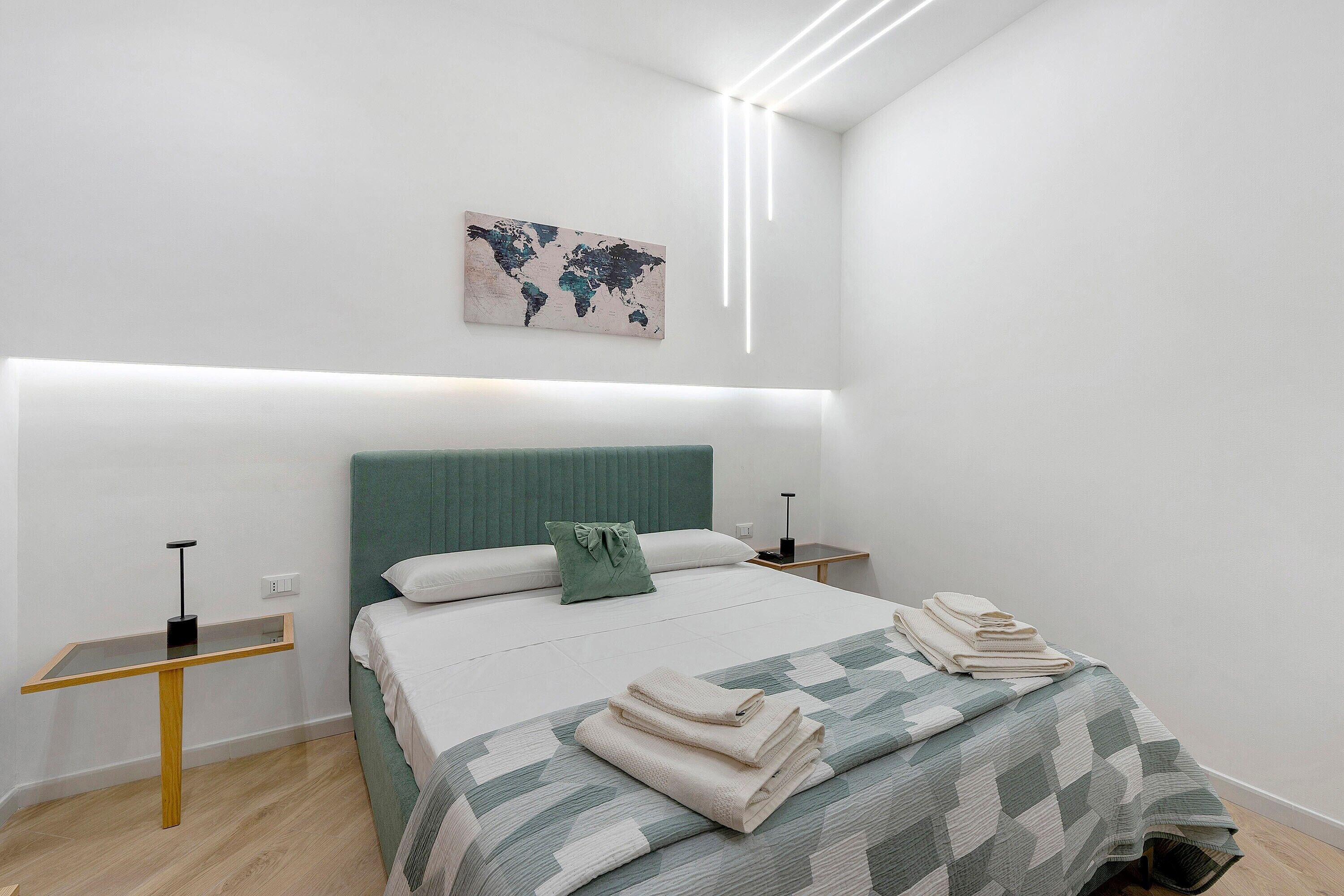Een moderne slaapkamer met een bed, een wereldkaart als kunstwerk, nachtkastjes en een bedlamp.