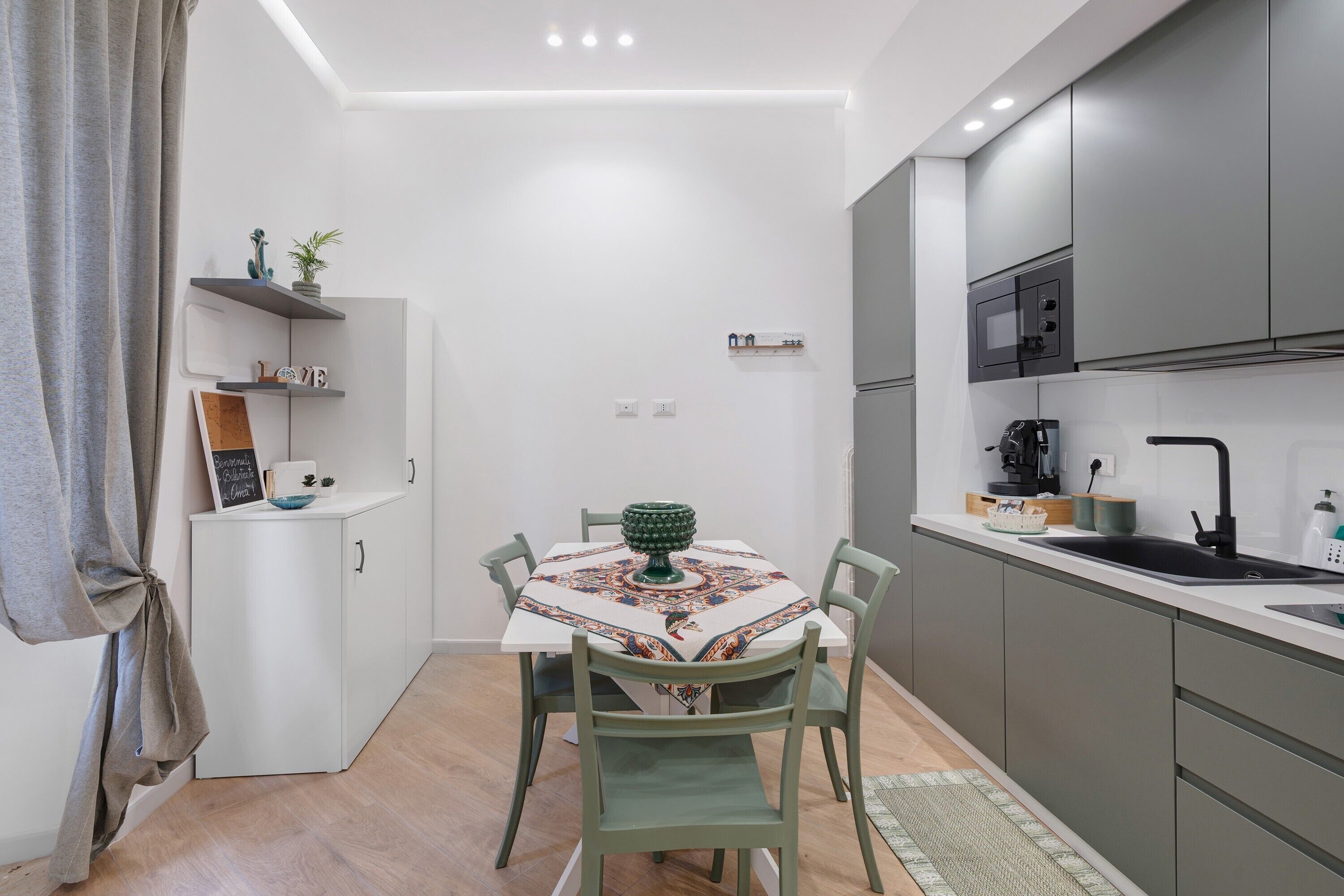 Een compacte keuken met moderne apparatuur, een eettafel met stoelen, en een klein eilandje met een decoratieve schaal.
