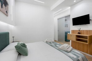 Une chambre d’hôtel moderne équipée d’un lit, d’un téléviseur à écran plat, d’une coiffeuse en bois et d’une grande fenêtre.
