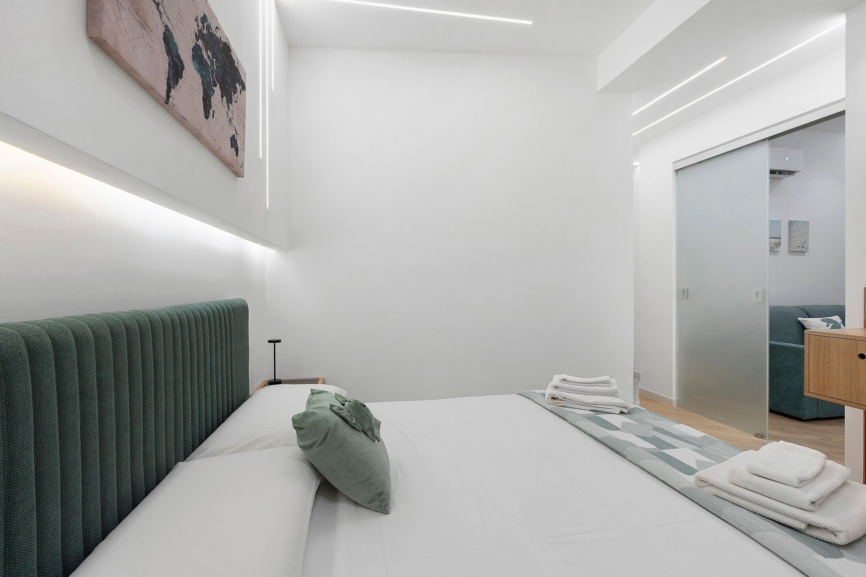 A modern hotel room with a neatly made bed, a green headboard, and a large mirror.