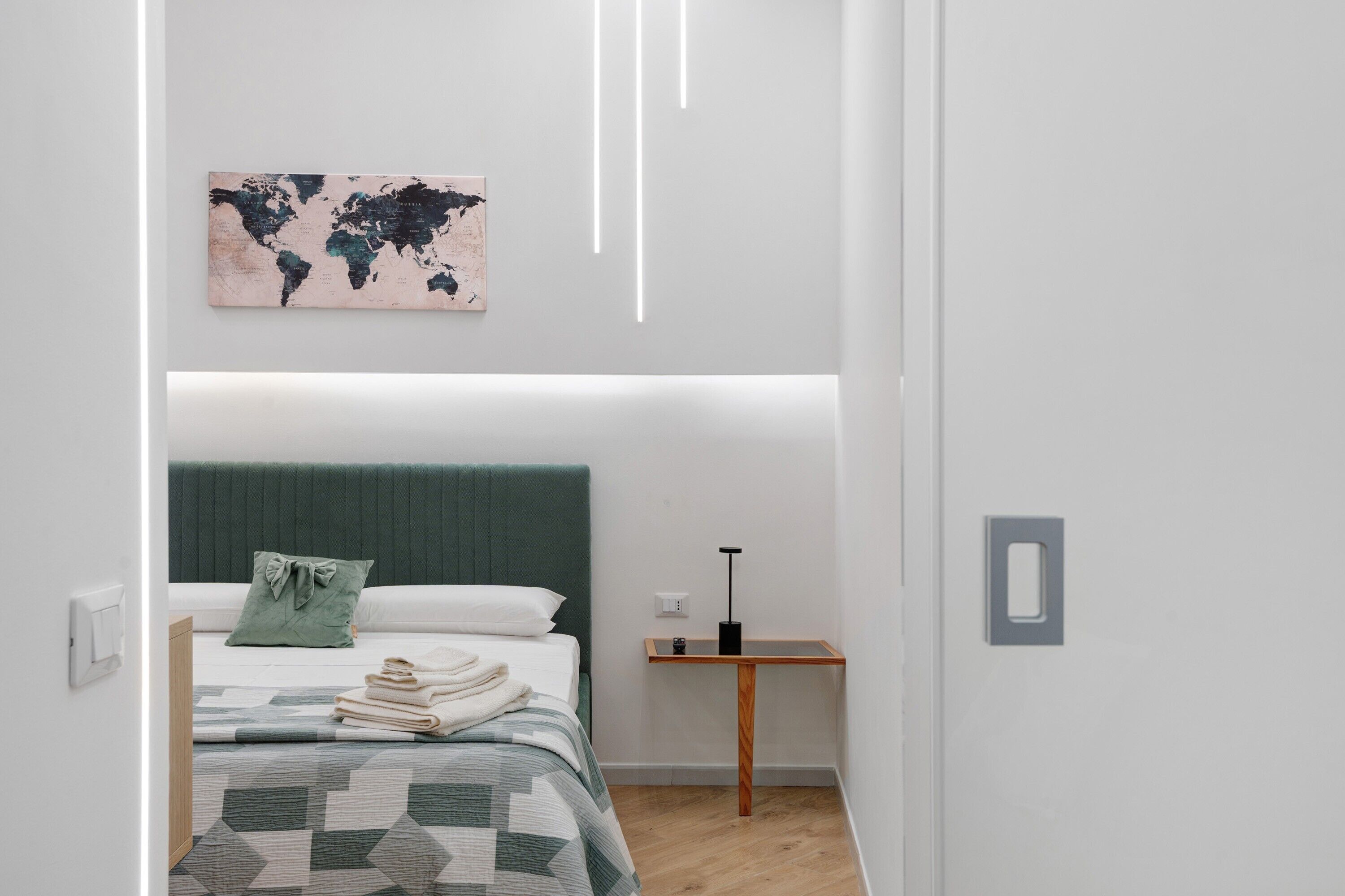 Ein schlicht eingerichtetes Schlafzimmer mit einem Bett, einer Weltkarte als Wandbild, einem Nachttisch und einer Lampe.