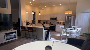 A modern kitchen with white cabinets, a central island, bar stools, and a dining area with a white table and chairs. - Minutes to the Sand! Pets! Charming 3-bedroom in beautiful Bradenton. (Bradenton)