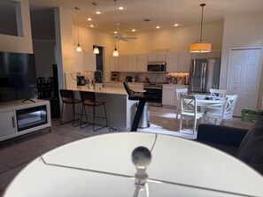 A modern kitchen with white cabinets, a central island, bar stools, and a dining area with a white table and chairs. - Minutes to the Sand! Pets! Charming 3-bedroom in beautiful Bradenton. (Bradenton)