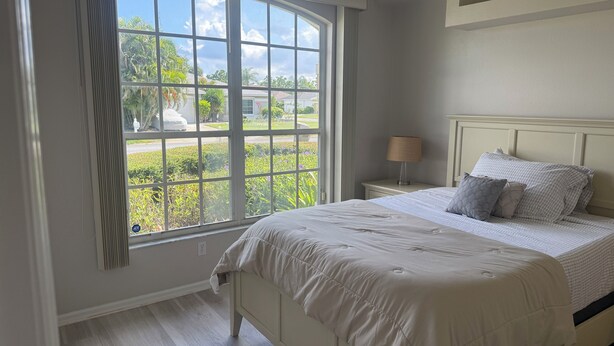 A bedroom with a large window, a bed with a white headboard, and a bedside table with a lamp. - Minutes to the Sand! Pets! Charming 3-bedroom in beautiful Bradenton. (Bradenton)