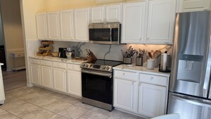 A kitchen with white cabinetry, a stainless steel refrigerator, a microwave, a stove, and a coffee maker. - Minutes to the Sand! Pets! Charming 3-bedroom in beautiful Bradenton. (Bradenton)