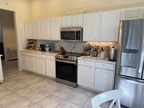 A kitchen with white cabinetry, a stainless steel refrigerator, a microwave, a stove, and a coffee maker. - Minutes to the Sand! Pets! Charming 3-bedroom in beautiful Bradenton. (Bradenton)